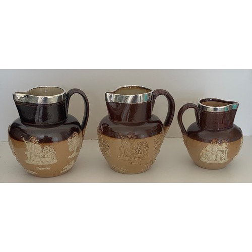 5 - A matched set of three Doulton Lambeth salt glazed and two tone jugs with silver collars, each with ... 