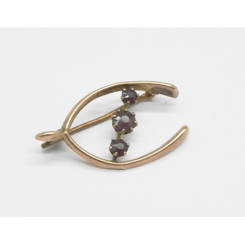 1075 - A 9ct gold and garnet wishbone brooch, 1.7g