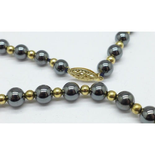 1064 - A gold and hematite bead necklace, the clasp marked 14kt