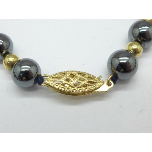 1064 - A gold and hematite bead necklace, the clasp marked 14kt