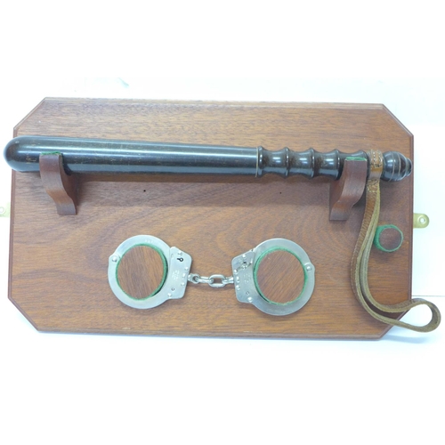 809 - A turned wooden truncheon and a set of handcuffs on a wooden mount