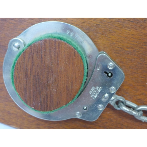 809 - A turned wooden truncheon and a set of handcuffs on a wooden mount