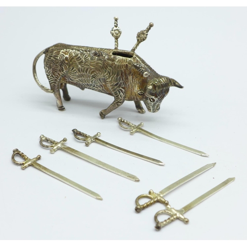 856 - A white metal stand in the form of a bull with six small swords/olive sticks, length 7.5cm