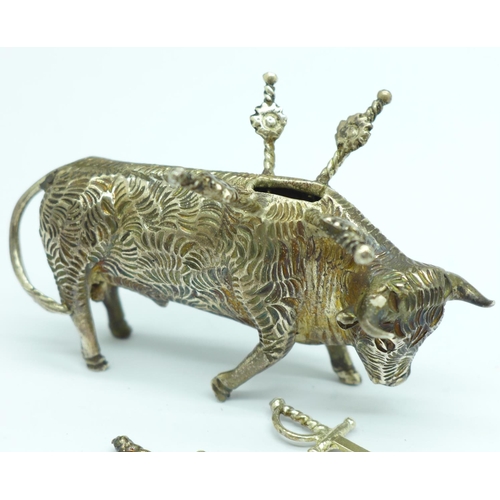 856 - A white metal stand in the form of a bull with six small swords/olive sticks, length 7.5cm