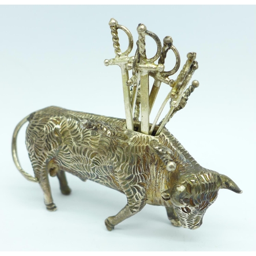 856 - A white metal stand in the form of a bull with six small swords/olive sticks, length 7.5cm