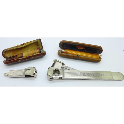 860 - Two cigar cutters and two amber cheroot holders, cased, one with 9ct gold rim a/f