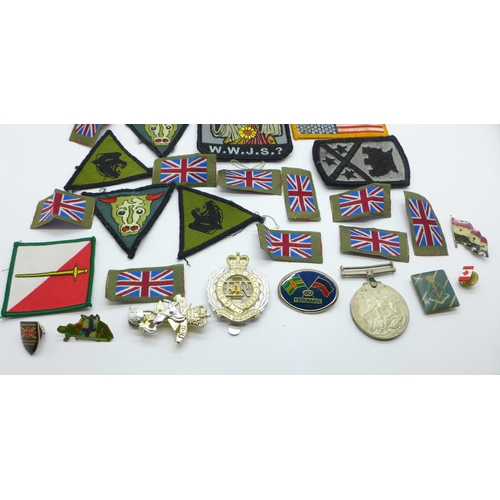 891 - A collection of cap badges, cloth badges, pin badges, etc., including a WWII medal