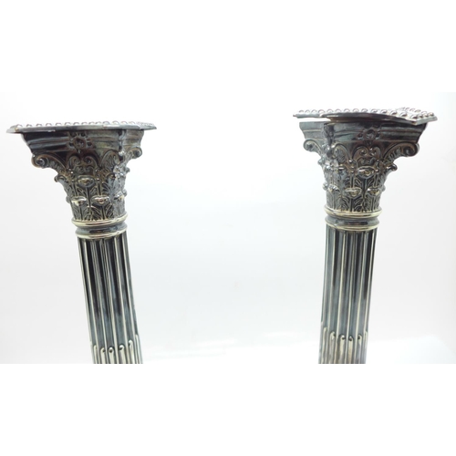 861 - A pair of silver candlesticks of reeded columnar form, with Corinthian tops, each on a square beaded... 