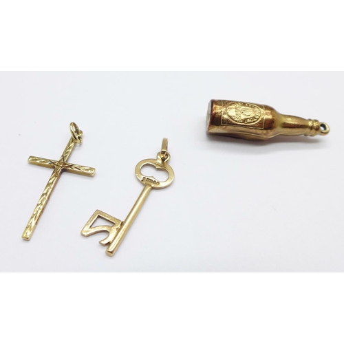 928 - Two 9ct gold charms and a 9ct gold cross pendant, Guinness bottle charm dented, 2.9g