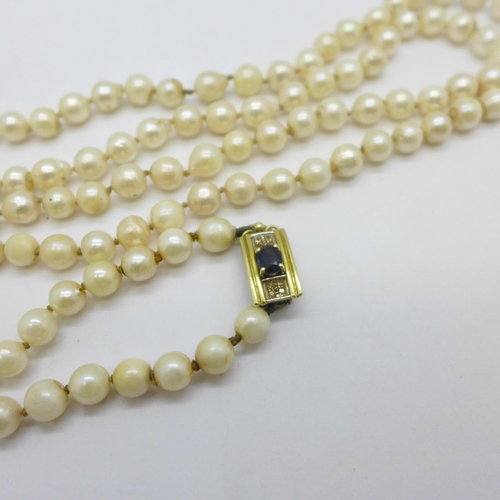 1013 - A string of cultured pearls with a 14ct gold clasp set with a sapphire, some pearls a/f, 86cm