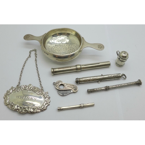 938 - A silver whisky label, a silver strainer, four pencils, a small silver pepper and a silver cutter