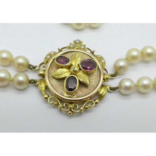 975 - A double row of cultured pearls with a 15ct gold clasp set with garnets, clasp 27mm x 33mm