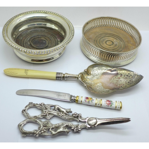 616 - A pair of plated grape scissors, two wine coasters, a server and a Royal Crown Derby knife