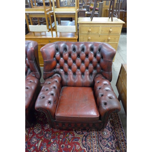 27 - A pair of oxblood red leather Chesterfield wingback armchairs