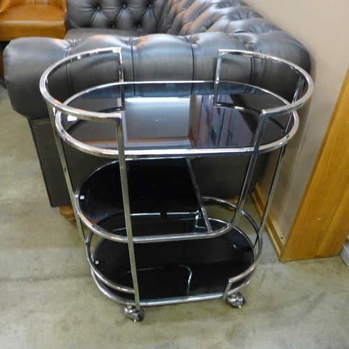 1360 - A pill shaped metal drinks trolley with black glass shelves  *This lot is subject to VAT