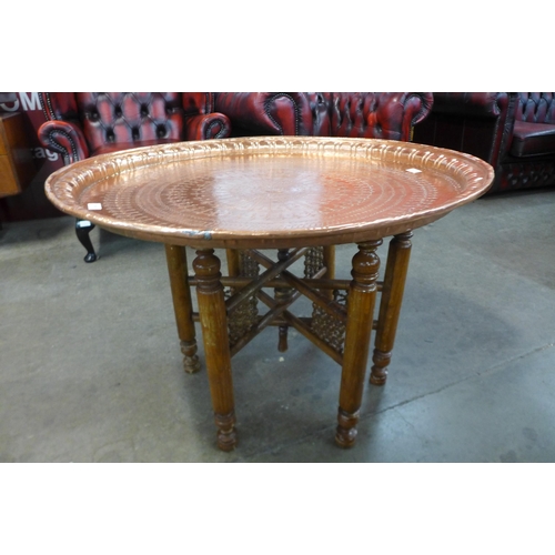 13 - An Egyptian copper coffee table, on carved hardwood folding base