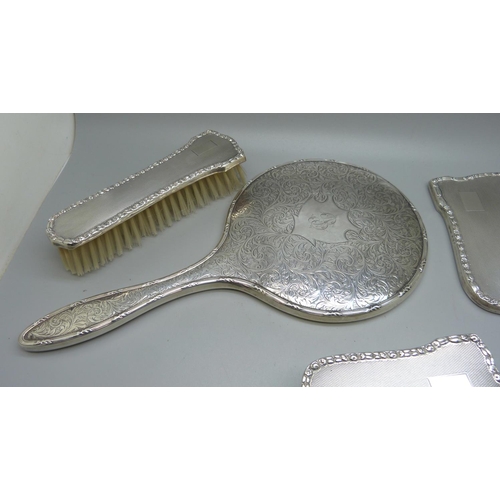 852 - A silver backed hand mirror with two matching brushes, one other silver backed hand mirror and a sil... 