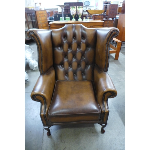 1 - A chestnut brown leather Chesterfield wingback armchair