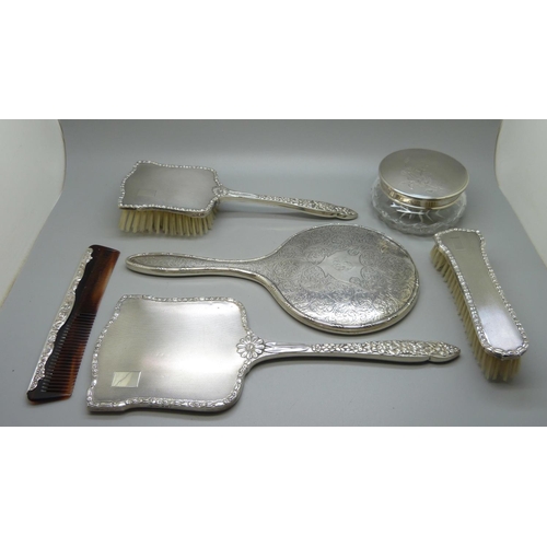 852 - A silver backed hand mirror with two matching brushes, one other silver backed hand mirror and a sil... 