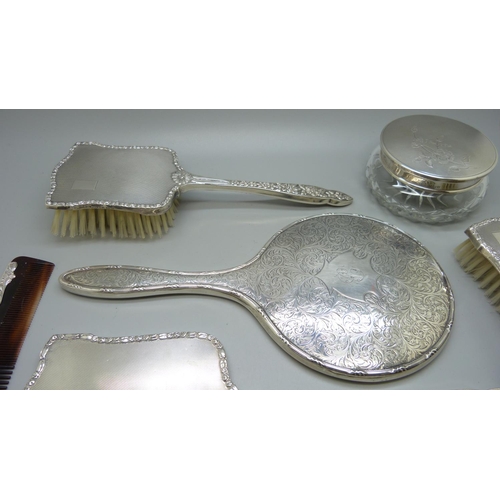 852 - A silver backed hand mirror with two matching brushes, one other silver backed hand mirror and a sil... 