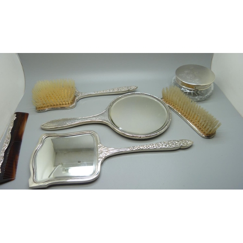 852 - A silver backed hand mirror with two matching brushes, one other silver backed hand mirror and a sil... 