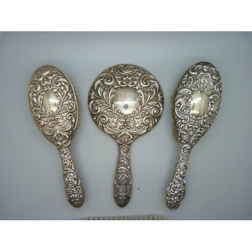 876 - A silver backed hand mirror and three brushes