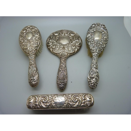 876 - A silver backed hand mirror and three brushes