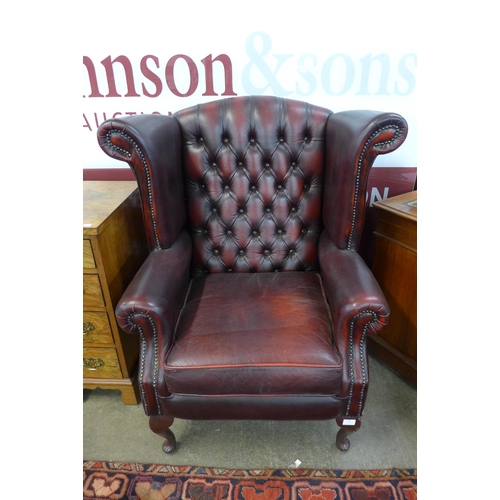 86 - An oxblood red leather Chesterfield wingback armchair