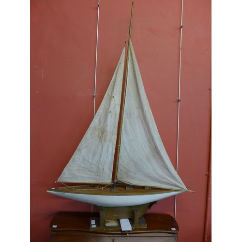 289 - A wooden Sam sized yacht, with canvas sail and display stand, 85cms l, 135cms h