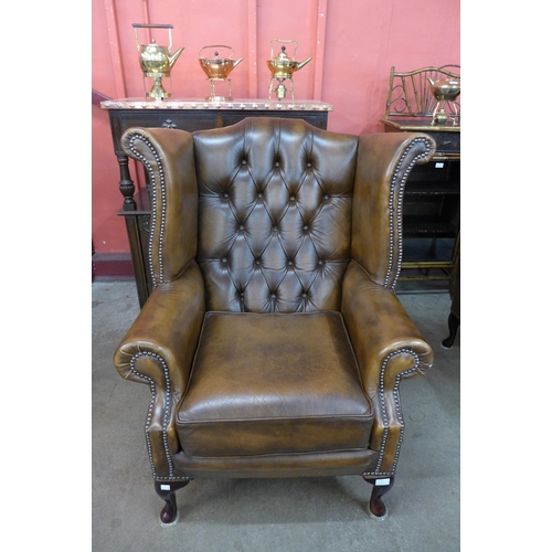 23 - A chestnut brown leather Chesterfield wingback armchair