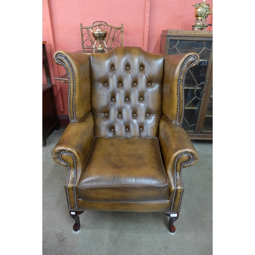 24 - A chestnut brown leather Chesterfield wingback armchair