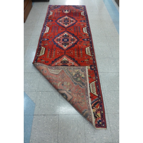 100 - An eastern red ground runner rug, 305 x 105cns