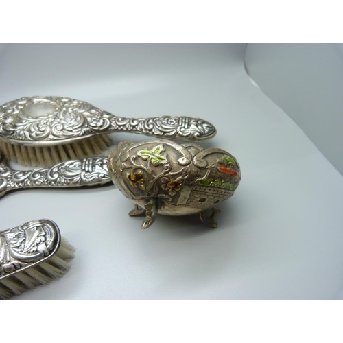 874 - A silver backed mirror and two brushes and a white metal and enamel pot