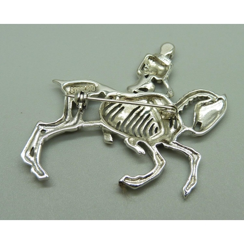 1082 - A silver brooch depicting a skeleton riding a horse, set with ruby eyes, 11g, 47mm