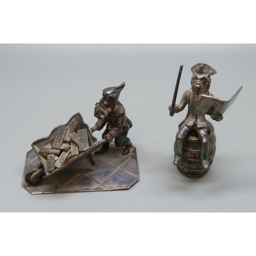 983 - Two silver figures; money seated on a barrel and a  Pixie pushing a wheelbarrow of gold, 107g