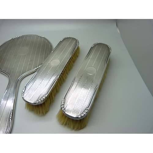 867 - An Art Deco silver backed vanity set; four brushes and a hand mirror