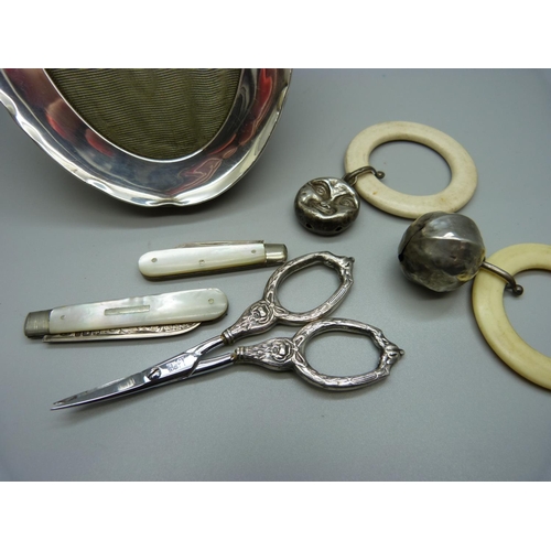 1031 - A silver frame, two rattles, scissors, two silver penknives