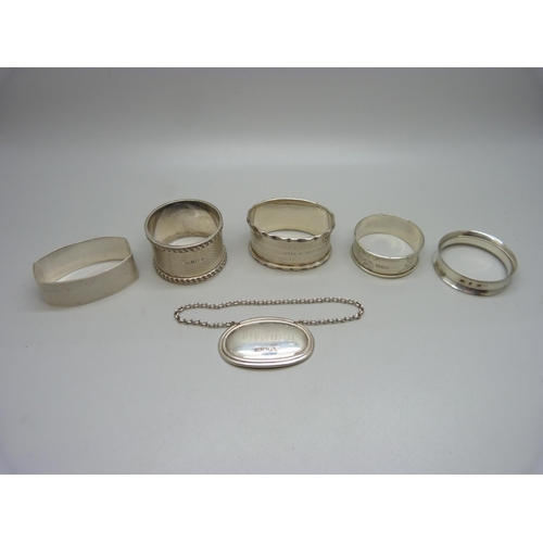 922 - Five silver serviette rings and a silver brandy label, 96g