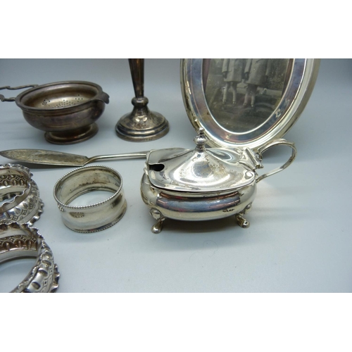 893 - A silver tea strainer and holder, three silver napkin rings, a silver butter knife, a silver mustard... 