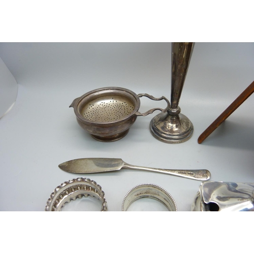 893 - A silver tea strainer and holder, three silver napkin rings, a silver butter knife, a silver mustard... 