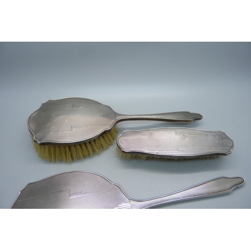 847 - A silver backed Art Deco hand mirror, Birmingham 1944 and two matching brushes, one a/f