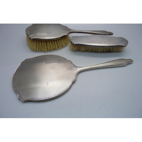 847 - A silver backed Art Deco hand mirror, Birmingham 1944 and two matching brushes, one a/f