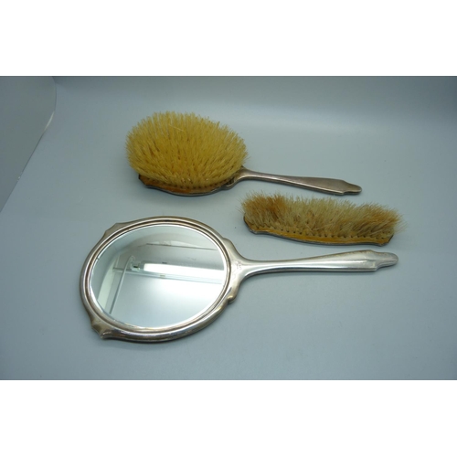 847 - A silver backed Art Deco hand mirror, Birmingham 1944 and two matching brushes, one a/f