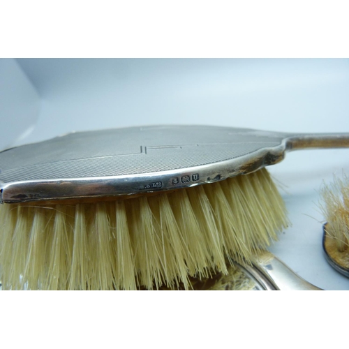 847 - A silver backed Art Deco hand mirror, Birmingham 1944 and two matching brushes, one a/f