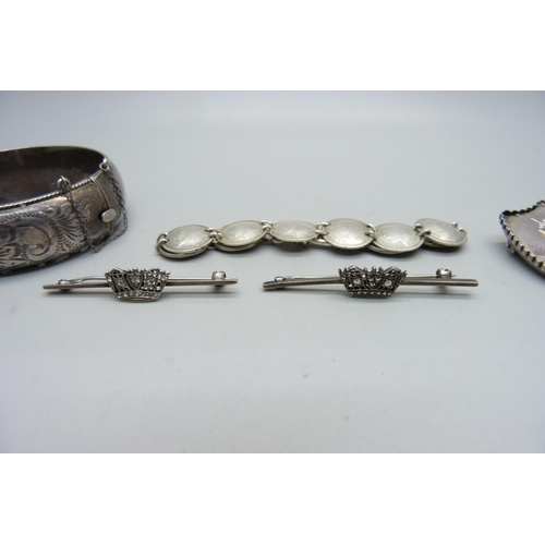 944 - A Victorian shield shaped brooch, two silver brooches, a silver bangle and a coin bracelet