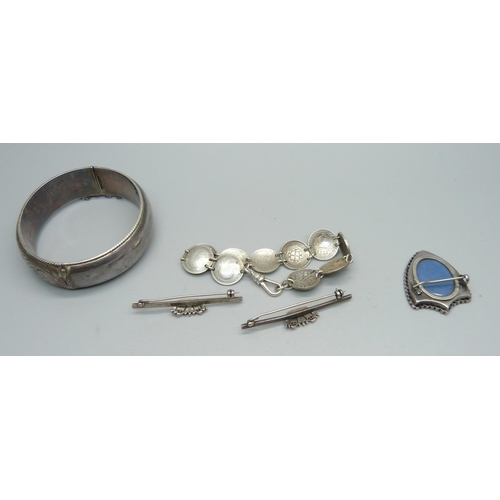 944 - A Victorian shield shaped brooch, two silver brooches, a silver bangle and a coin bracelet