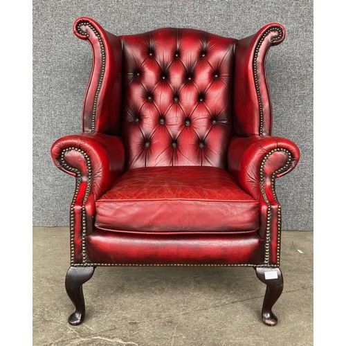 120 - An oxblood red leather Chesterfield wingback armchair