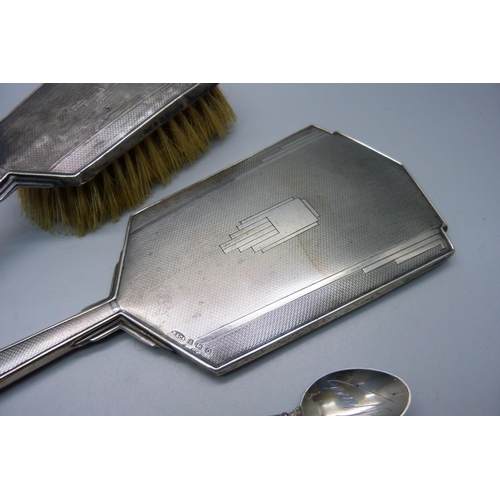 863 - A silver backed Art Deco hand mirror, a brush, a hallmarked silver spoon and nine white metal spoons... 