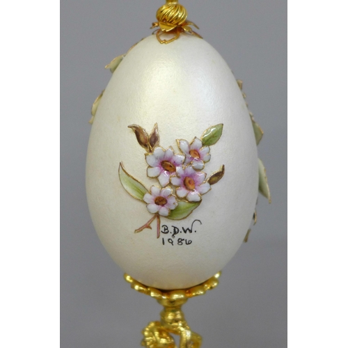 673 - A hand decorated egg on stand, with glass dome