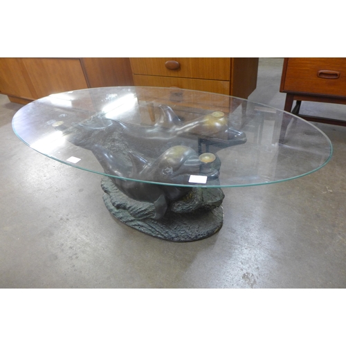 130 - An oval glass topped coffee table, on faux bronze dolphin base